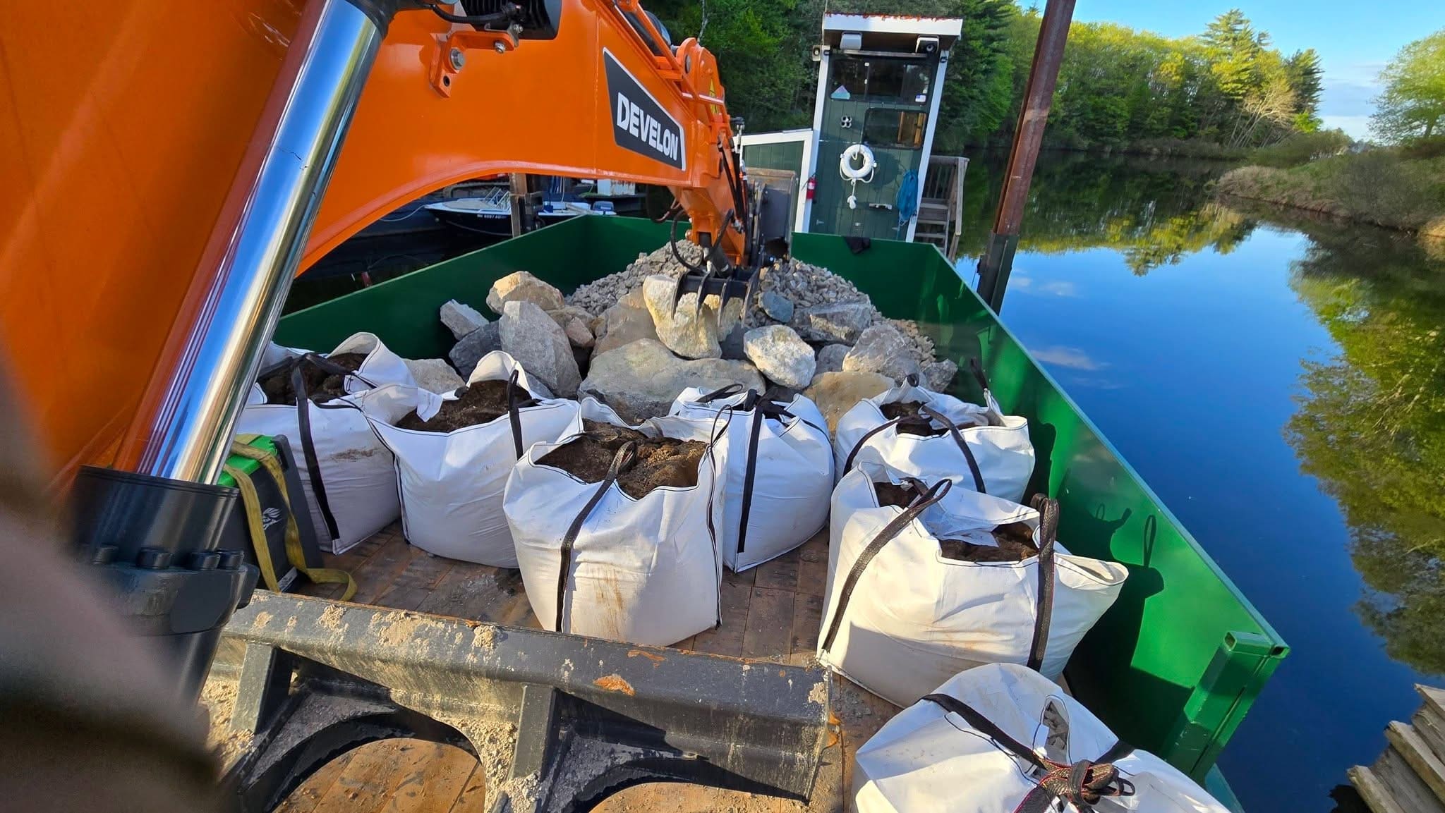 Excavator with super-sack rip-rap stones loaded on a barge