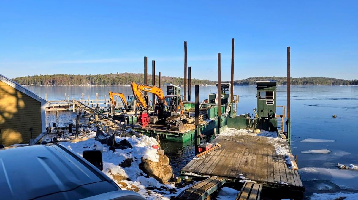 Two excavators on a green barge with mountains in the distance