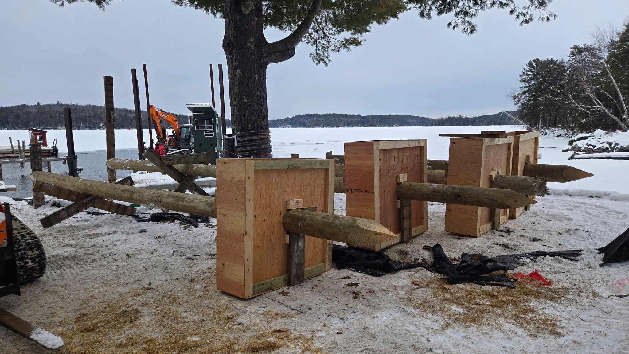 Dock framing with newly cut piles staged on shore beside the frozen lake