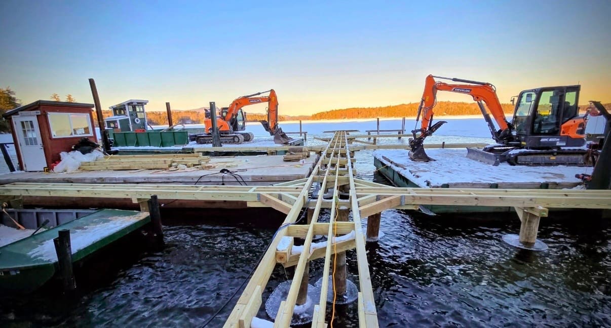 Twin excavators on barges silhouetted at golden hour over a frozen lake